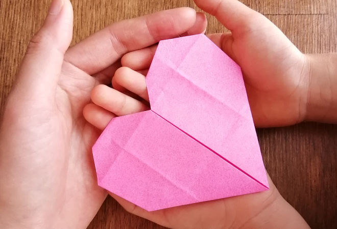 母と幼い娘の手のひらの中にある、ハートの折り紙の写真。