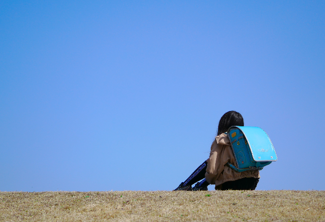 ランドセルを背負って土手に座り込んでいる子どもの写真。