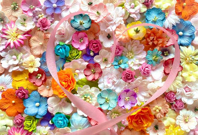 ハート型になるように置かれたピンクのリボンと明るい色の花の写真。